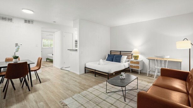 Une pièce moderne et bien éclairée, comprenant un lit, une table à manger avec des chaises, une table basse, un bureau avec une lampe et un canapé.