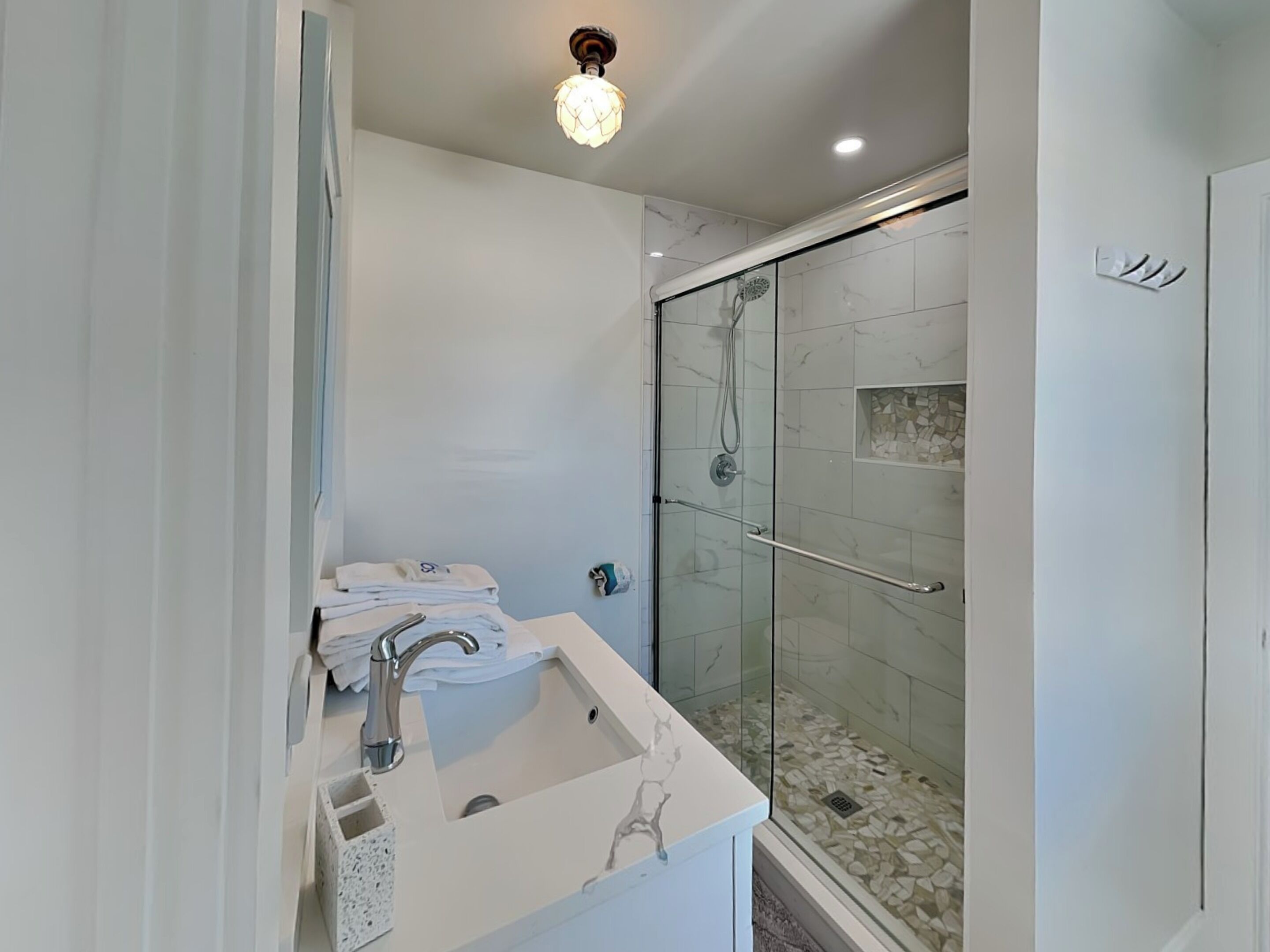 A modern bathroom with a glass-enclosed shower, a white sink with a marble design, and a ceiling light fixture.