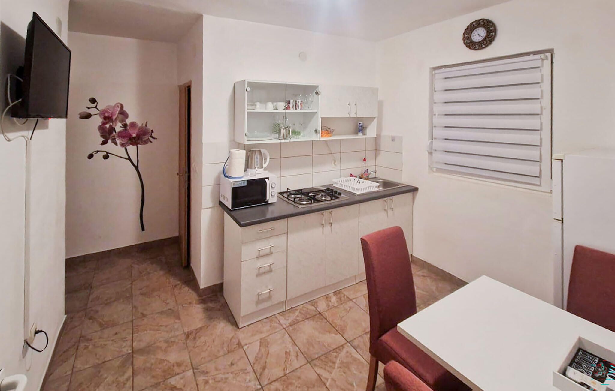 Cocina compacta con microondas, tostadora y estufa a gas. Hay una mesa de comedor con sillas y un televisor pequeño montado en la pared.