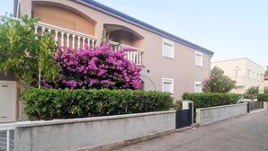 Ein Wohngebäude mit Balkon, einer Betonmauer und einem kleinen Garten mit rosa Blüten.