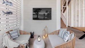Un intérieur moderne avec un mur blanc, un tableau représentant un paysage en noir et blanc encadré, des meubles en osier et un escalier avec des rampes blanches.