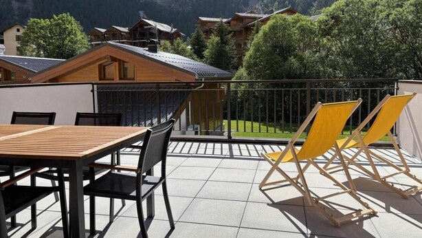 Una terrazza con tavolo e sedie, vista su una zona montuosa con edifici tradizionali.