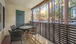 Un balcon avec des meubles en osier, une porte et une vue sur les arbres et les bâtiments.