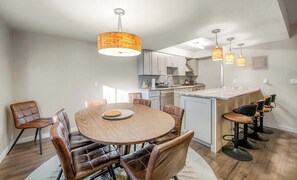Une cuisine moderne dotée d’un îlot central, d’un coin repas avec une table ronde et des chaises en cuir, et d’un éclairage suspendu.
