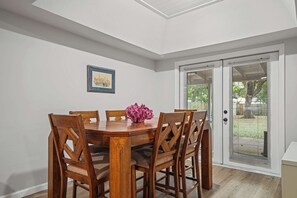 Un coin repas avec une table et des chaises en bois, un tableau encadré au mur et une porte-fenêtre coulissante donnant sur un espace extérieur.