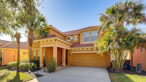 A two-story house with a garage, surrounded by palm trees and a well-maintained lawn. - Poolside Living: Family Retreat 12 Mi to Disney (Davenport)