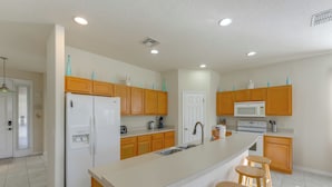 A modern kitchen with wooden cabinets, a white refrigerator, a microwave, and a large island with stools. - Poolside Living: Family Retreat 12 Mi to Disney (Davenport)