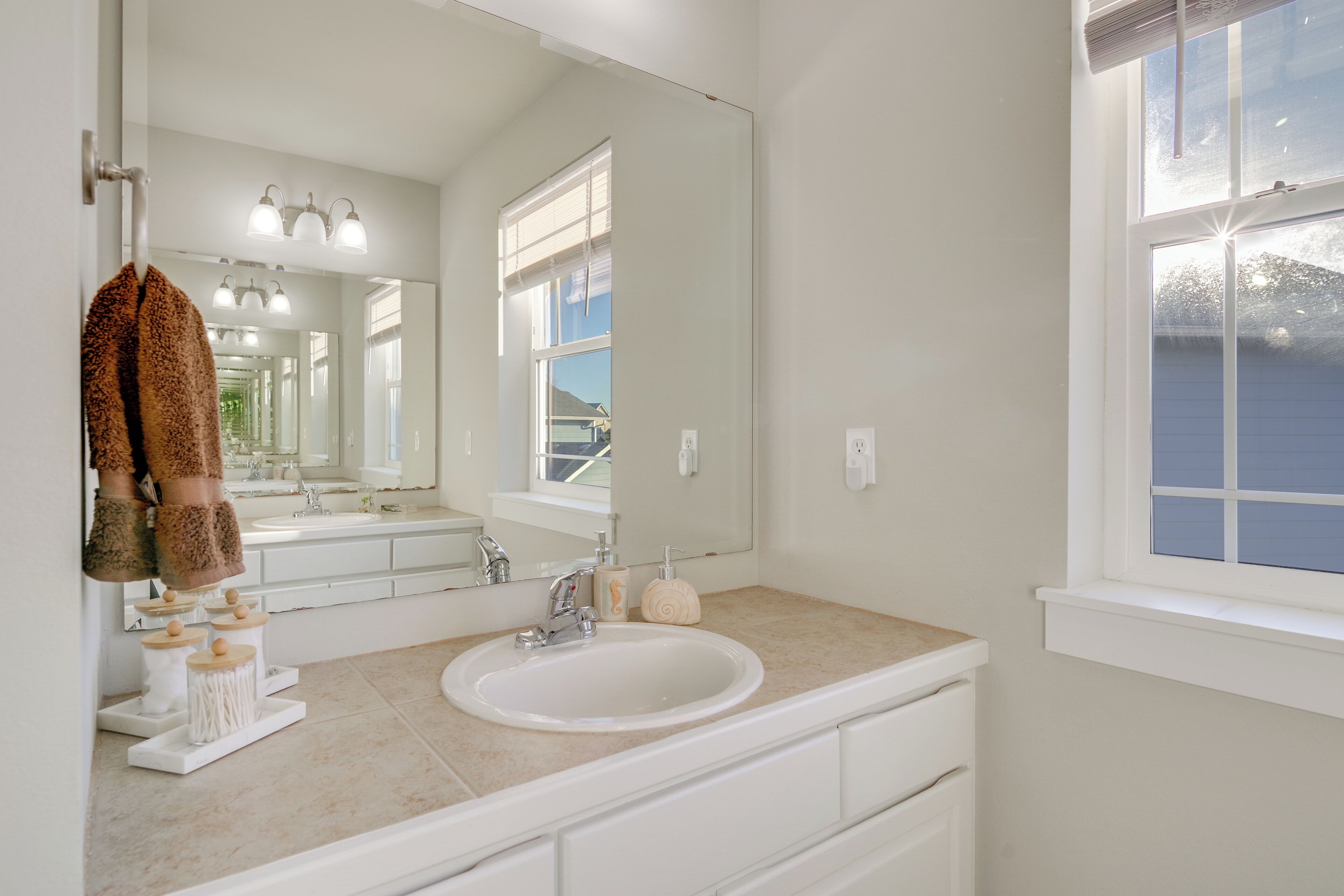 A bathroom with a white sink, a large mirror, and a window.