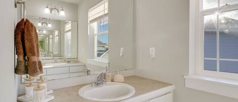 A bathroom with a white sink, a large mirror, and a window.