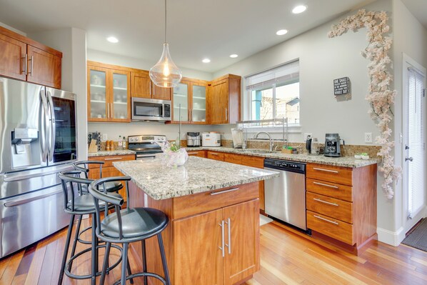 A modern kitchen with wooden cabinets, stainless steel appliances, granite countertops, and a central island with bar stools.