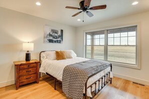 Une chambre à coucher comprenant un lit, une table de chevet, un ventilateur de plafond, une fenêtre et un tableau accroché au mur.