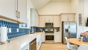 A modern kitchen with white cabinets, a stainless steel refrigerator, a microwave, and a stove. There is a wooden dining table with chairs and a vase of flowers. - Lake Greenwood Access: Modern Escape w/ Patio! (Greenwood)