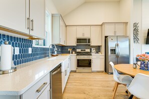 Eine moderne Küche mit weißen Schränken, einem Edelstahl-Kühlschrank, einer Mikrowelle und einem Herd. Ein Holztisch mit Stühlen und eine Blumenvase stehen bereit.
