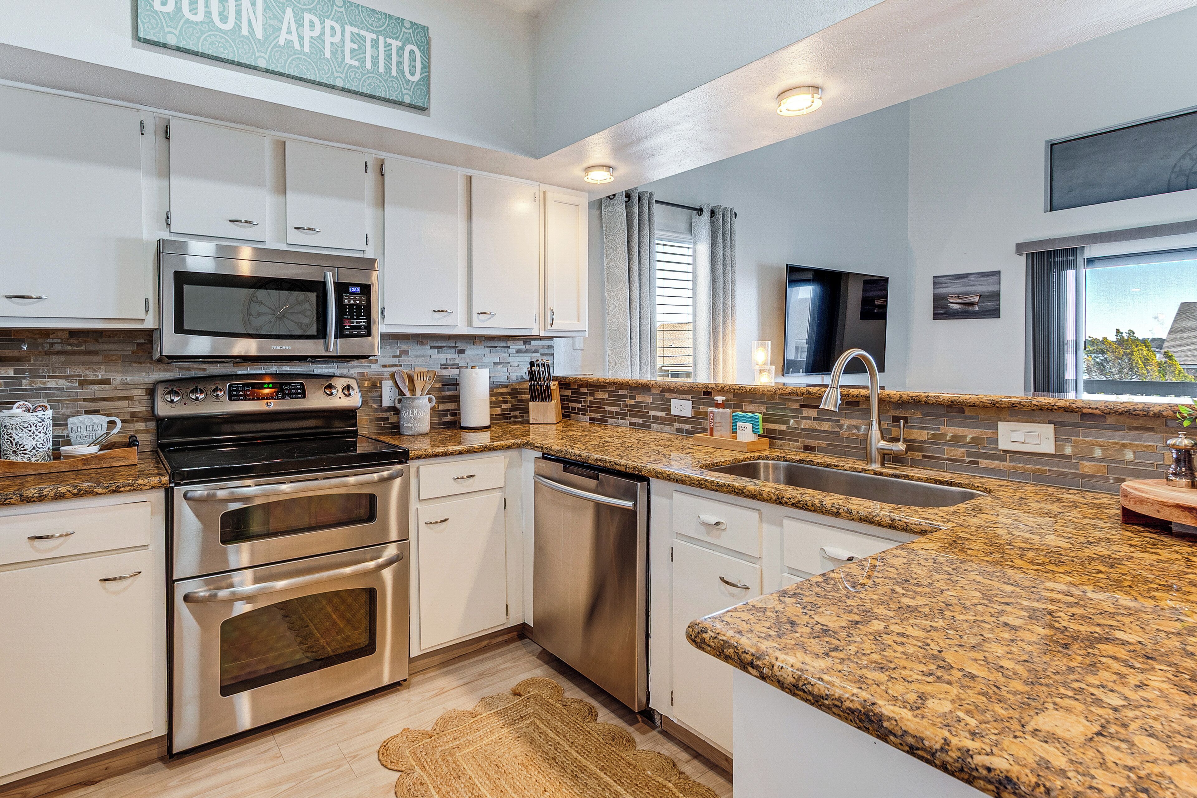 A modern kitchen with stainless steel appliances, granite countertops, and a large window providing natural light.