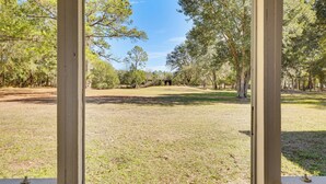 A view through a window of a grassy area with trees and a distant structure. - Wooded Couple's Retreat w/ Lanai in Interlachen (Interlachen)