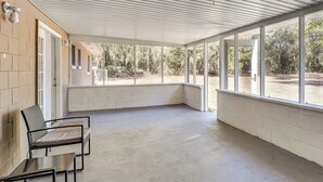 A covered outdoor area with a concrete floor, white brick walls, and large windows offering a view of the surrounding trees. - Wooded Couple's Retreat w/ Lanai in Interlachen (Interlachen)