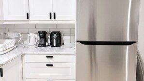 Cuina moderna amb armaris blancs, un refrigerador d'acer inoxidable, una cafetera i un brollador a la superfície.