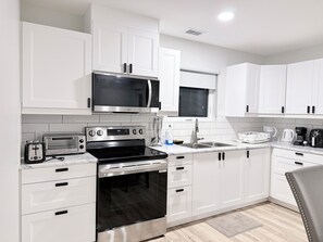 A modern kitchen with white cabinets, a microwave, a toaster, an oven, and a sink.
