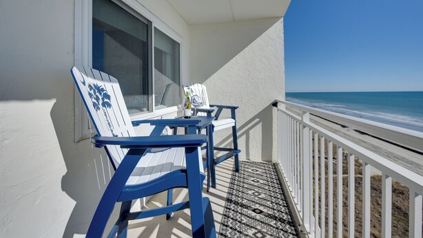 Un balcone con due poltrone Adirondack blu e bianche, un tavolino e una bottiglia di vino.
