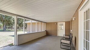 A covered outdoor area with a concrete floor, a white ceiling, and a door leading to a building. There are two chairs and a small table. - Hike & Fish! Wooded Family Getaway in Interlachen (Interlachen)