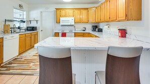 A modern kitchen with wooden cabinets, a white countertop, and a built-in oven. There are two bar stools and a large island. - Hike & Fish! Wooded Family Getaway in Interlachen (Interlachen)