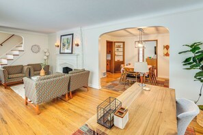 Uma sala de estar com lareira, móveis estampados, uma área de jantar com mesa de madeira e uma escada.