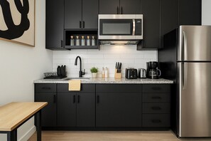 Een moderne keuken met donkere kastjes, een roestvrijstalen koelkast, een magnetron en een granieten aanrecht.