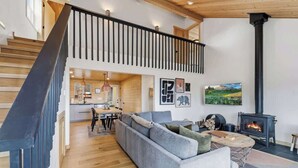A spacious living area with a high ceiling, a staircase, a fireplace, and a dining area.