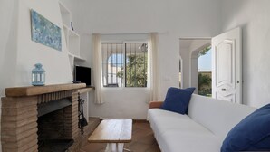 A room with a fireplace, a sofa, a table, and a window with curtains. - Rural House 'Casas Pepe 2' with Private Terrace, Wi-Fi, and Air Conditioning (Los Caños de Meca)