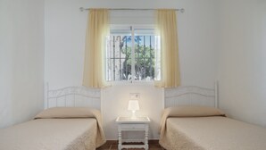A room with two beds, a window with curtains, a nightstand with a lamp, and a view of trees outside. - Rural House 'Casas Pepe 2' with Private Terrace, Wi-Fi, and Air Conditioning (Los Caños de Meca)