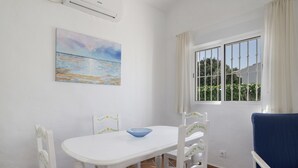 A room with a white table, chairs, a blue cushion, a painting, and a window with curtains. - Rural House 'Casas Pepe 2' with Private Terrace, Wi-Fi, and Air Conditioning (Los Caños de Meca)