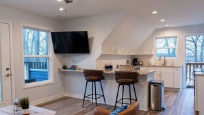 A modern kitchen with a TV, bar stools, and a trash can. - The Blue Herron of Carpenters Lake (Maceo)