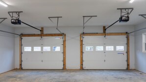 Un garage spacieux doté de deux grandes portes, d’un éclairage fixé au plafond et d’un sol en béton.