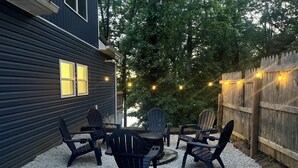 Une terrasse avec des fauteuils Adirondack et une table, entourée d’une clôture en bois et d’arbres.