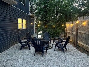 A patio with Adirondack chairs and a table, surrounded by a wooden fence and trees.