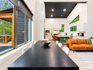 A modern kitchen with white cabinets, a dining area with a black table, and a living room with an orange sofa. - Pine Retreat | Hot Tub | Fire Pit Swings & Arcade (Broken Bow)