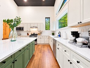 A modern kitchen with white cabinets, a wooden floor, and a large island with a vase of greenery. - Pine Retreat | Hot Tub | Fire Pit Swings & Arcade (Broken Bow)