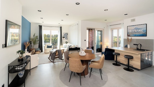 Eine moderne Küche mit Kochinsel, ein Essbereich mit rundem Tisch und ein Wohnbereich mit Sofa und Fernseher.