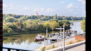 Ein Fluss mit an einem Yachthafen vertäuten Booten, umgeben von üppiger Vegetation und einem in der Ferne liegenden Gebäude mit rotem Dach.