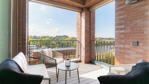 Ein Balkon mit einer Couch, einem runden Tisch und Blick auf einen Fluss und Bäume.