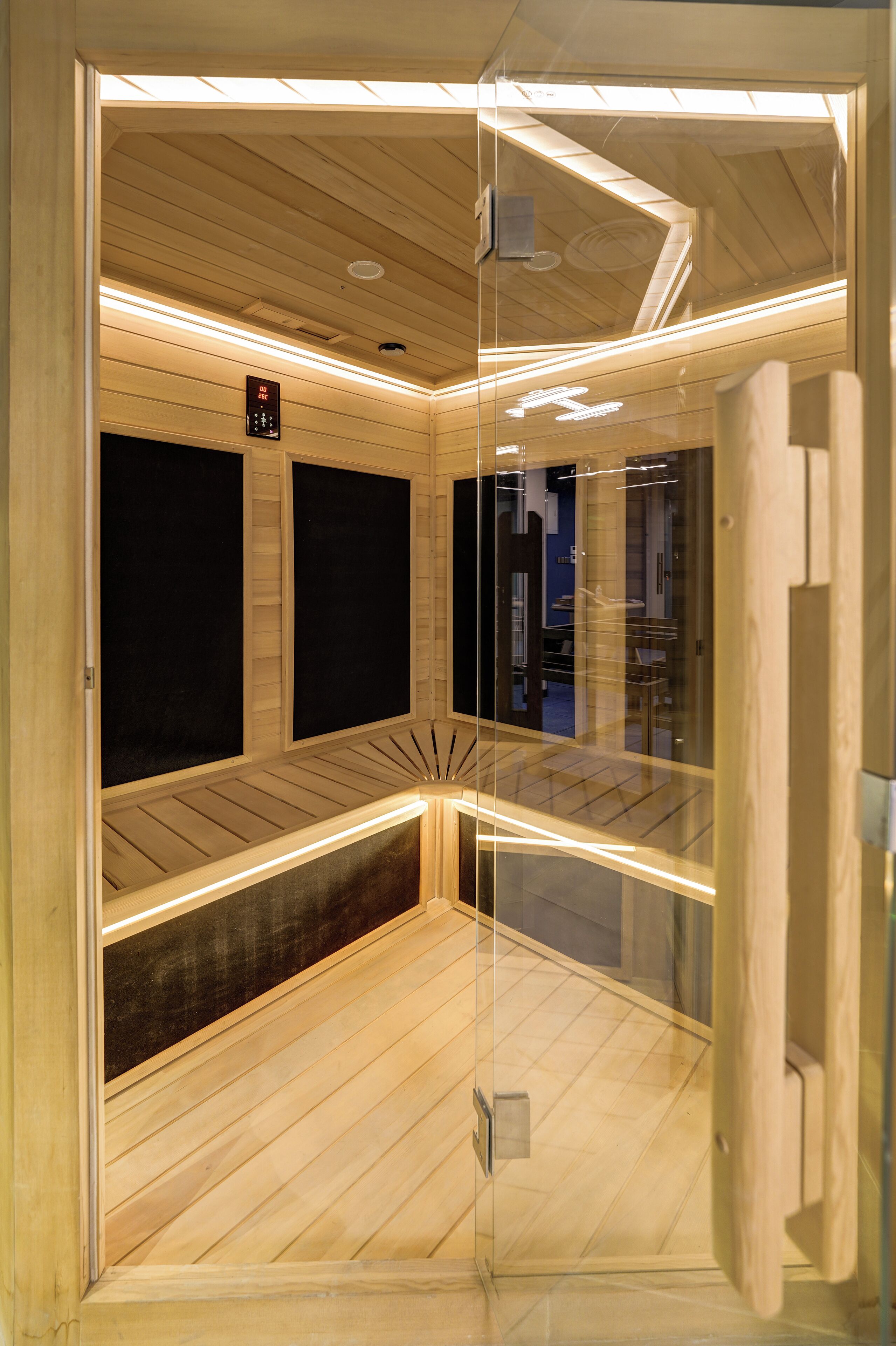 A sauna room with wooden walls and ceiling, glass doors, and a control panel.