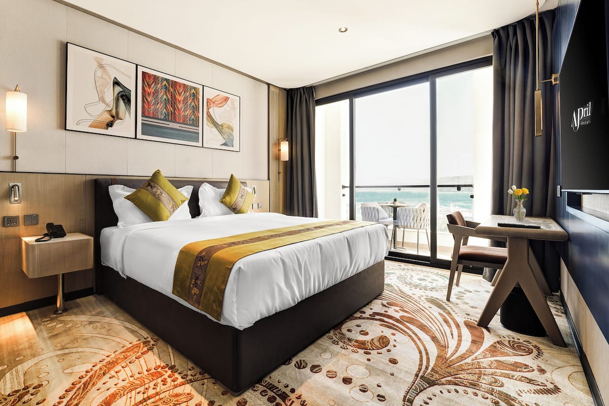 A hotel room with a large bed, a desk, and a view of the sea.