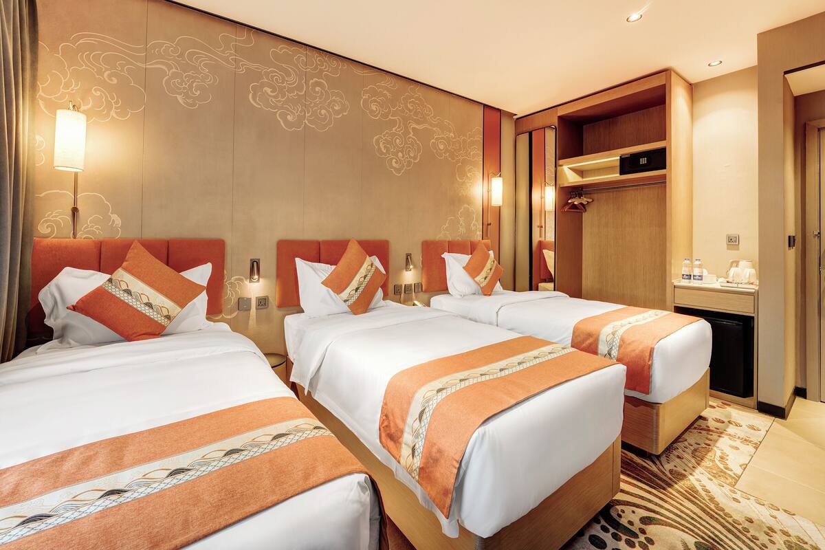 A hotel room with three beds, a minibar, and a shower area.