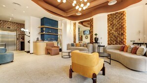 Un salon moderne avec un canapé, un fauteuil et une table basse. Il y a également un coin cuisine équipé d’un réfrigérateur et d’étagères.