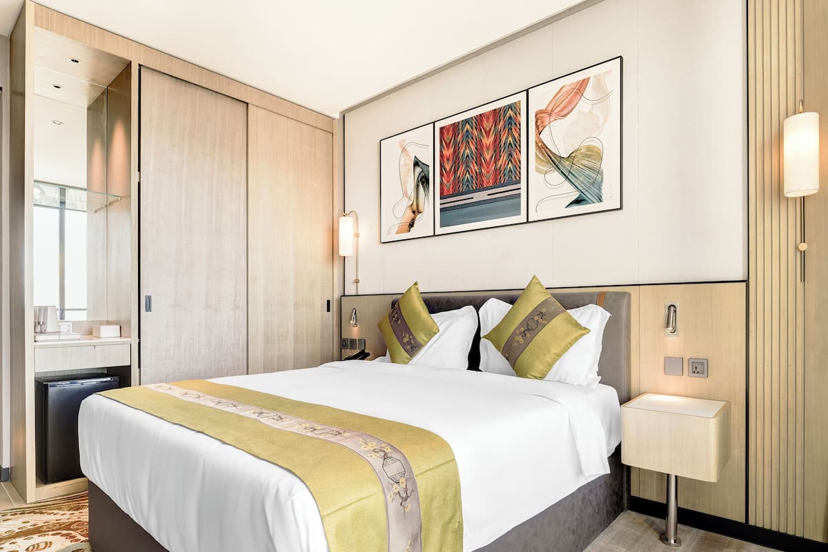 A hotel room with a bed, bedside table, wall art, and a wardrobe.