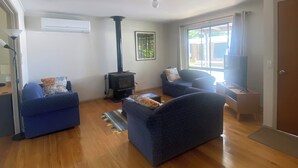 Ein Wohnzimmer mit zwei blauen Sofas, Holzboden, Kamin und einem großen Fenster.