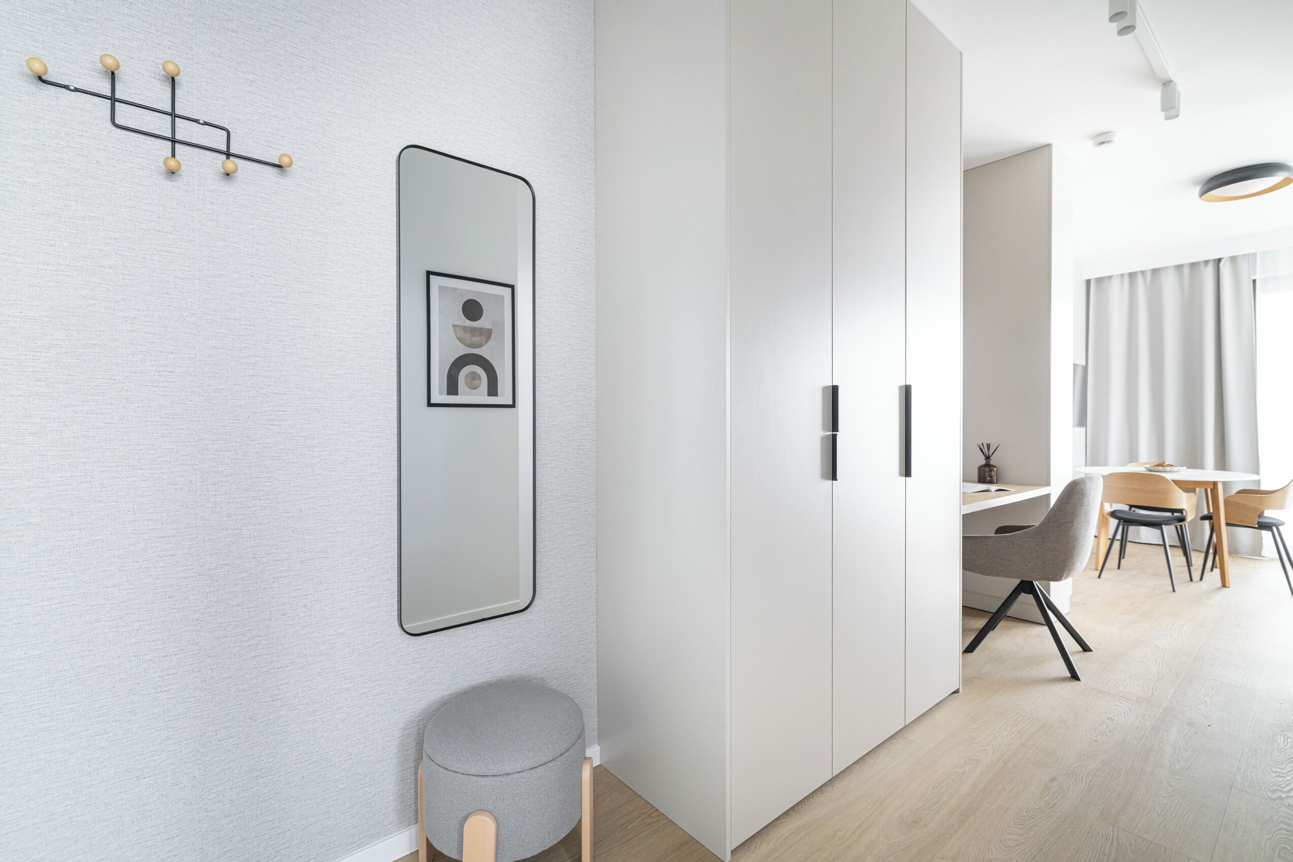 Una habitación moderna y minimalista con un espejo grande, una pequeña mesa redonda y un comedor con sillas.