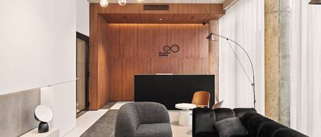 Un vestíbulo moderno con un mostrador de recepción de madera, un sofá negro, un sillón gris y una mesa redonda.