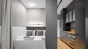 Ein modernes Hotelzimmer mit einem großen Bett, einem Nachttisch, einem Einbauofen und einer kleinen Küchenzeile.