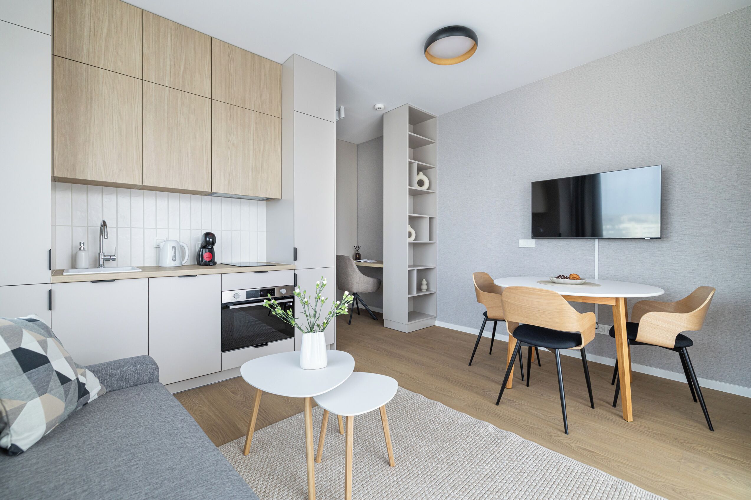 Una cucina moderna con mobili bianchi, un'area pranzo con tavolo e sedie rotonde, e un televisore piatto montato a parete.